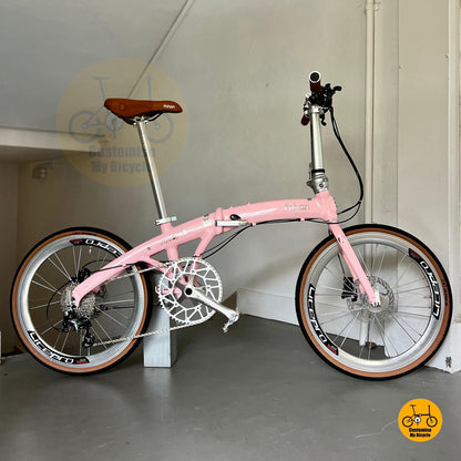 Pink bicycle with brown seat on a stand against a plain wall.