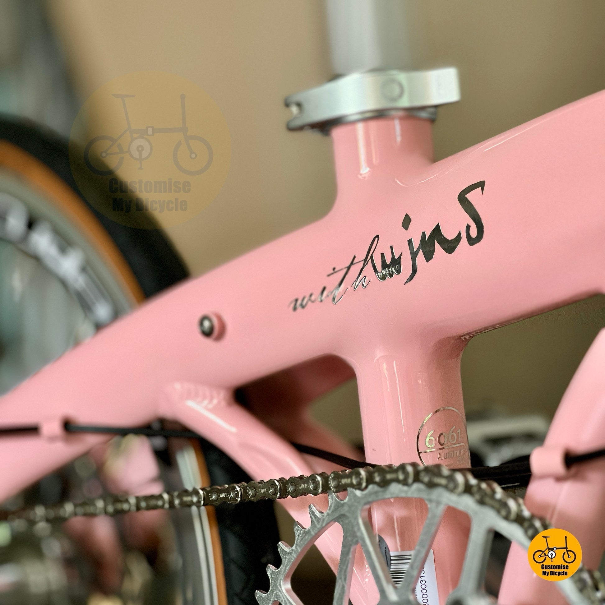 Close-up of a pink bicycle frame with 'with wind' written on it, blurred background
